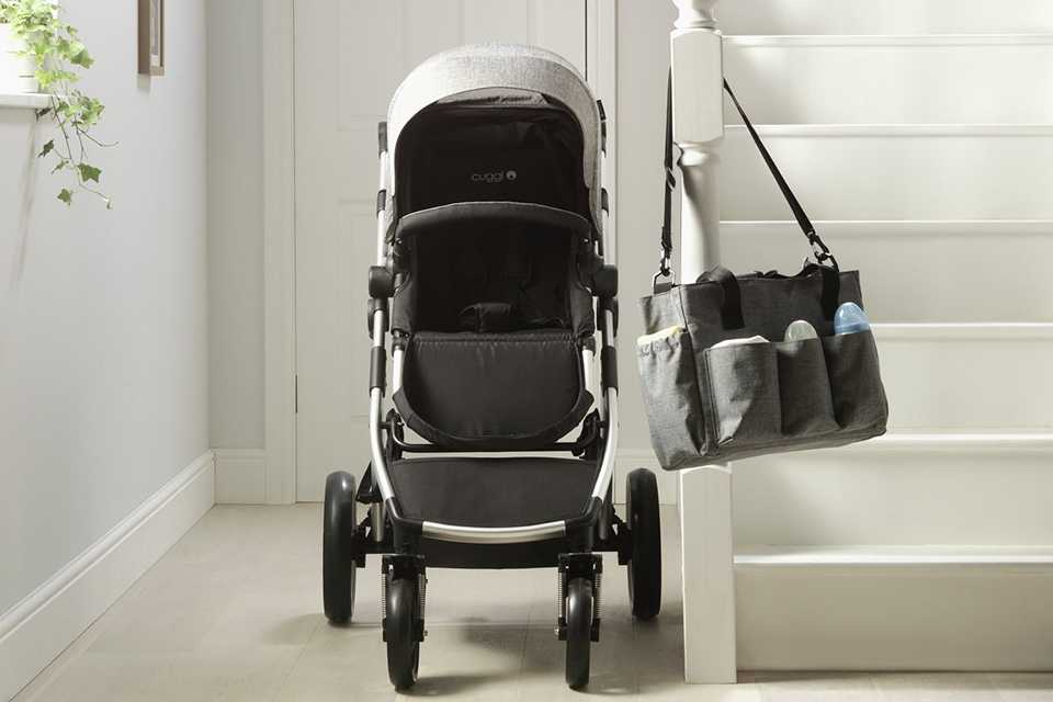 A Cuggl pushchair next to a staircase with a black bag hanging from it.