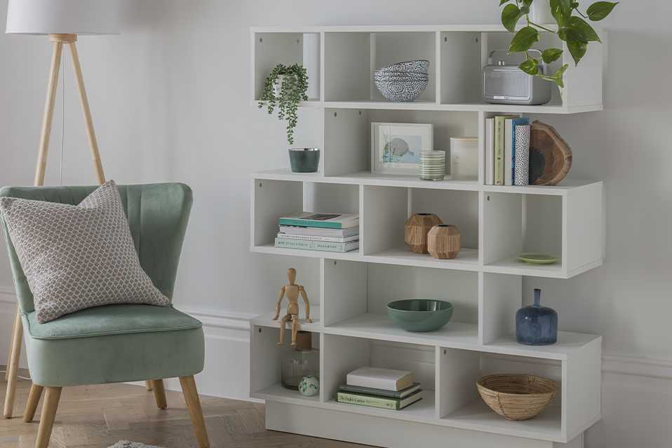 A tiered white cube bookcase beside a duck-egg green accent chair against a white wall.