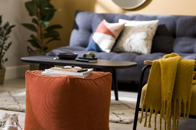 An orange footstool surrounded by mid-century style furniture and accessories.