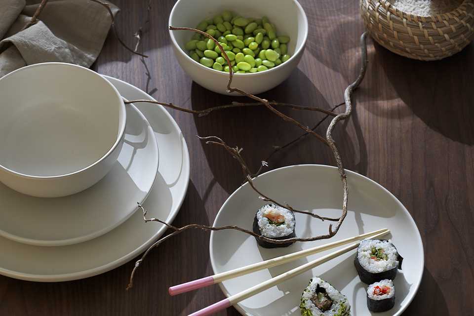 Simplistic cream stoneware on a wooden table with sushi and pastel-tipped chopsticks.