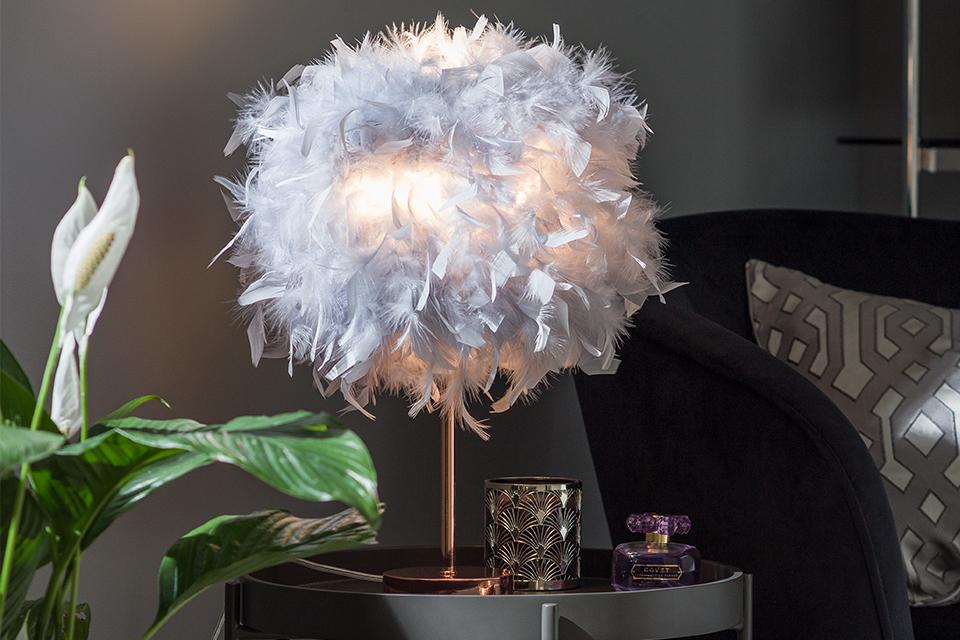 Image of a chrome table lamp with a grey feather shade on a side table next to a black chair.