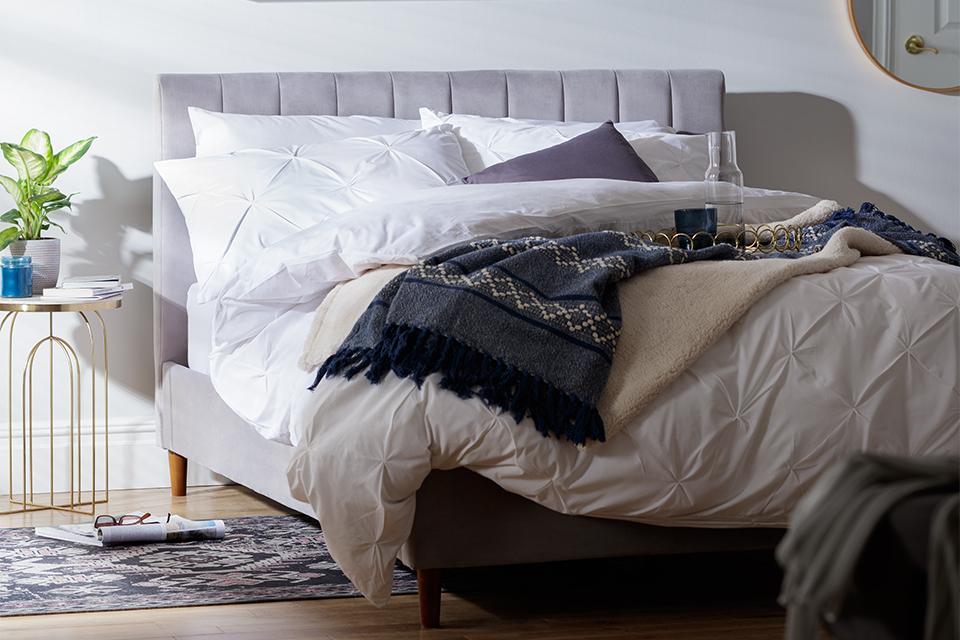 Image of a bed with white bedding an a lilac headboard.