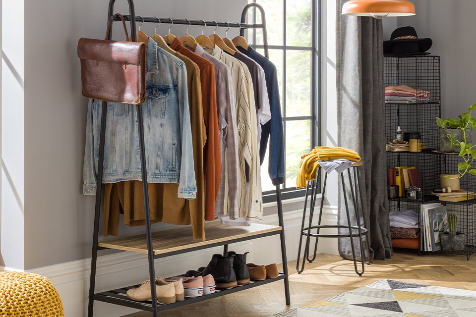 Black clothes rail with wooden slatted shelf on bottom filled with clothes.