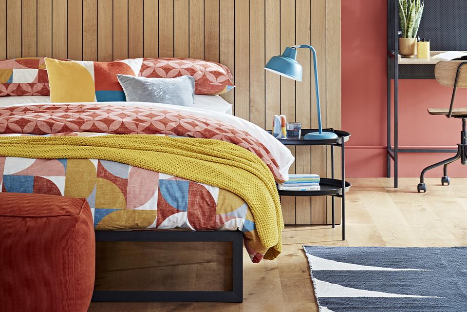 Image of a bedroom with a wooden and orange walls and colourful bedding.
