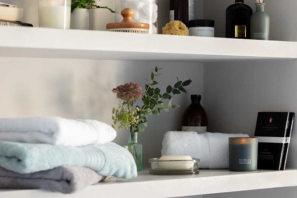 A close-up of white bathroom shelving unit with ornaments and towels. 