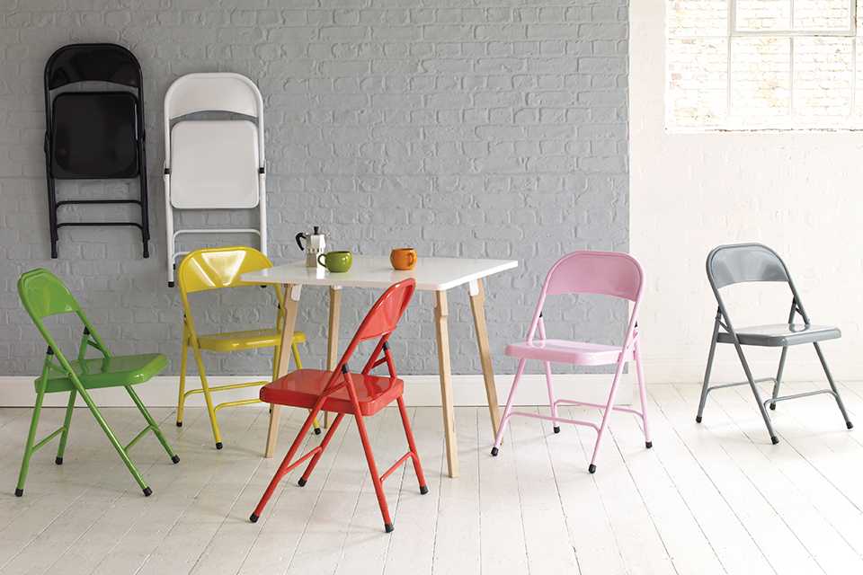 Brightly coloured folding chairs around a square white dining table.