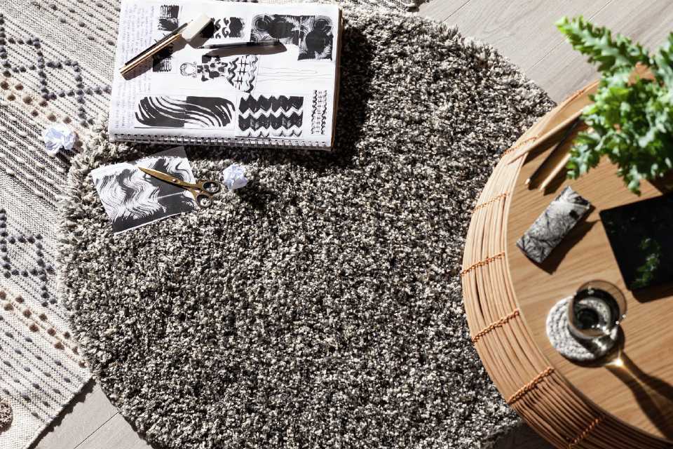 A thickly woven speckled rug beside a round bamboo side table.