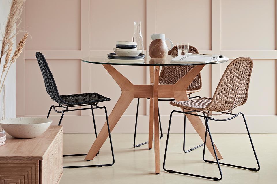 Three black and brown rattan chairs around a glass topped wooden dining table.