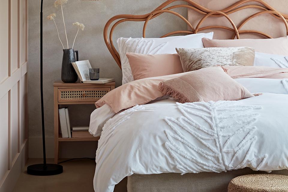 A artisan styled bedroom with white, textured bedding and muted pastel cushions and throws.
