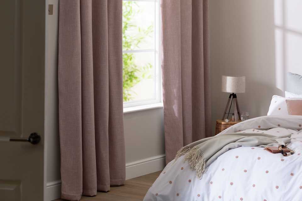 Pink linen curtains in a bedroom with spotty bed linen.