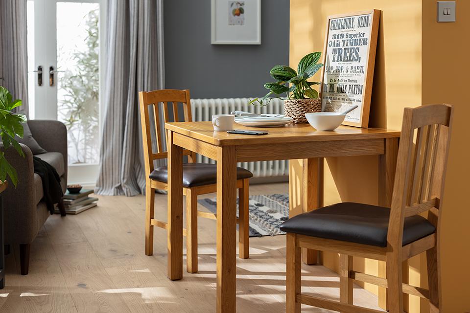 A square dining table and two matching chairs in a grey and orange living space.