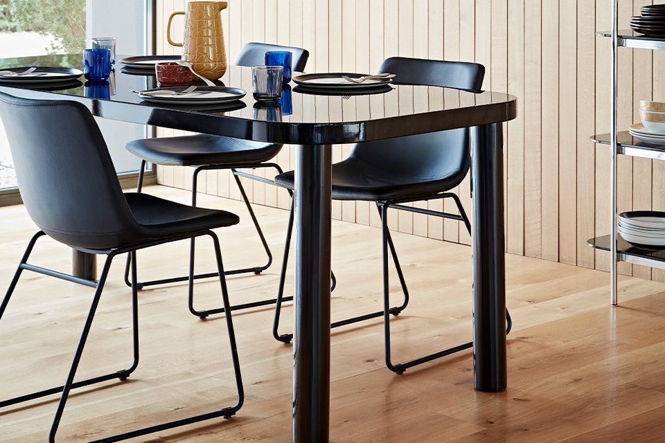 A black dining table with a glass top and rounded corners with black mid-century style chairs.