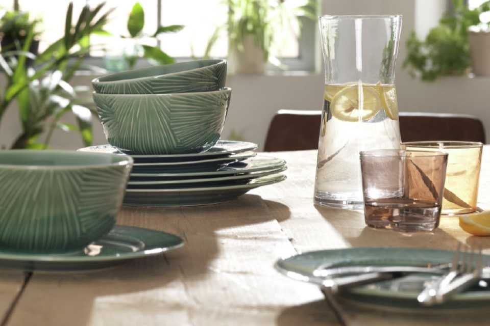 A textured set of green bowls and plates on an oak table with glassware.