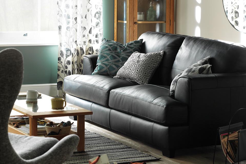 A black leather sofa with mismatched cushions in a cream and green living room.