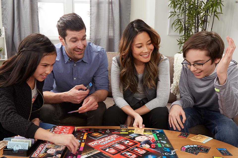 A family of four playing Monopoly Cheaters Edition on a large coffee table.