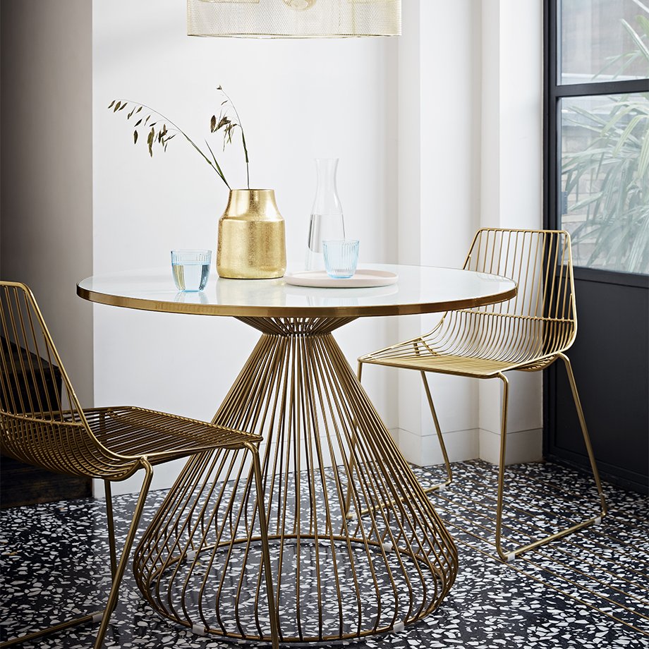 A gold and glass-topped round dining table with matching chairs and decor.