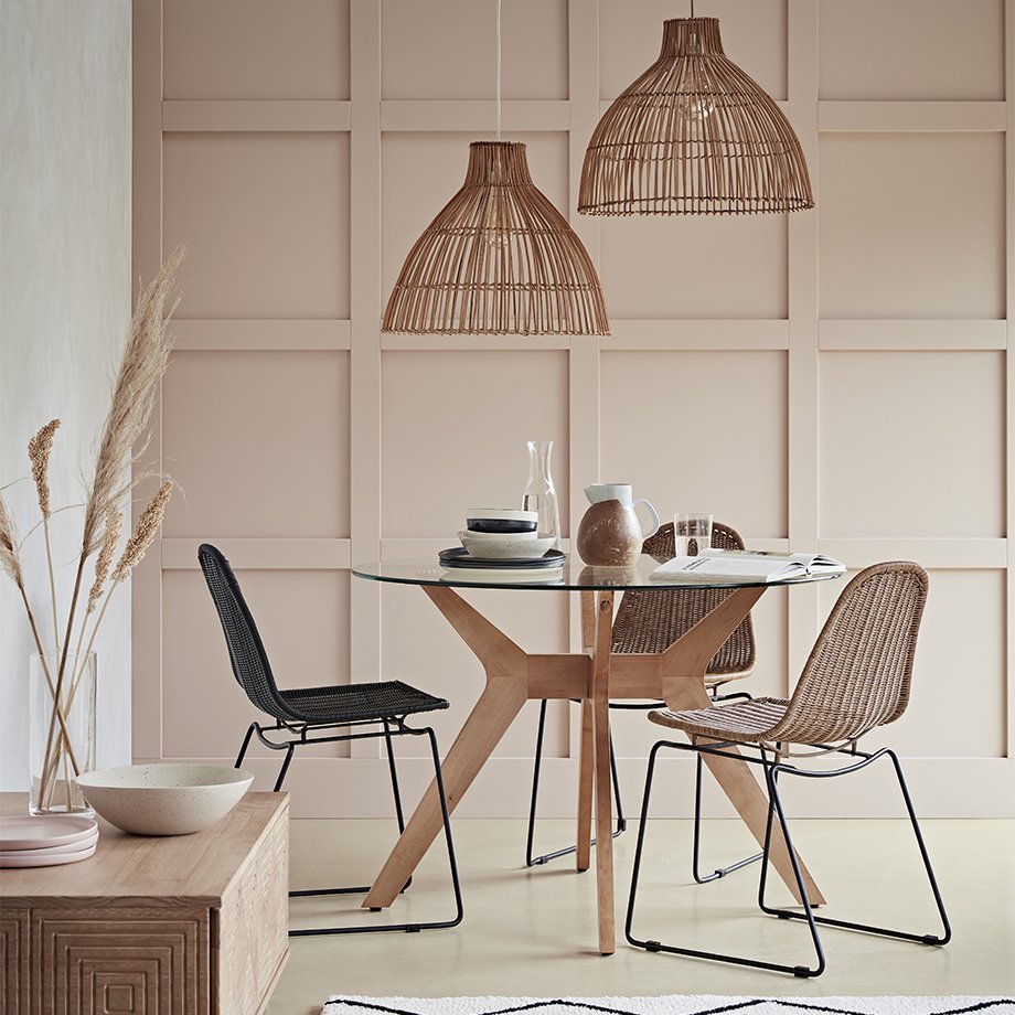 A round glass table with brown and black rattan chairs and matching decor.