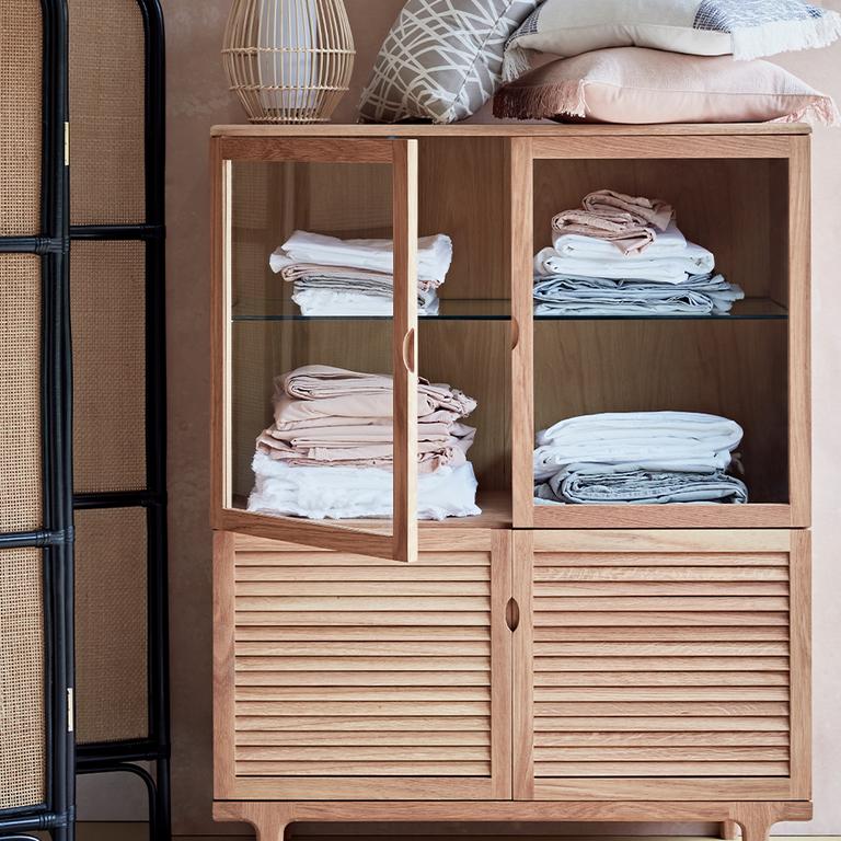 Image of a wooden storage unit with towels inside and cushions stored on top.