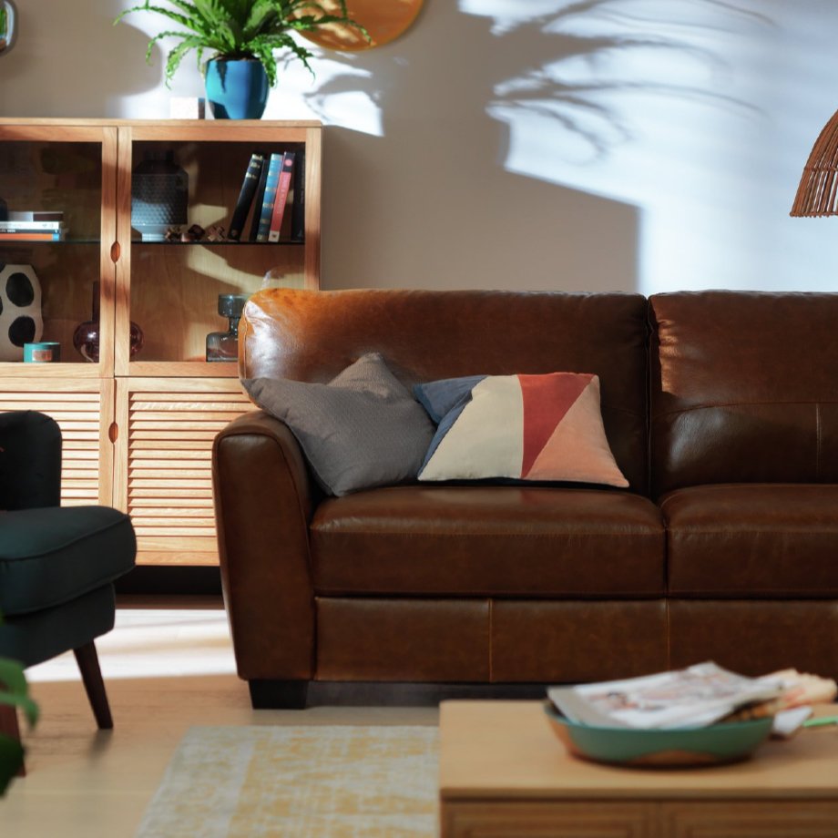 A brown leather sofa with mismatching cushions.