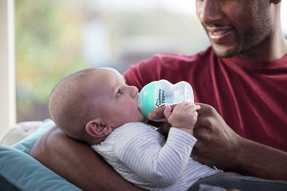 A baby being bottle-fed by a man.