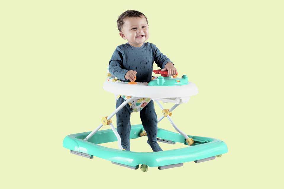A smiling baby uses a green Chad Valley baby walker.