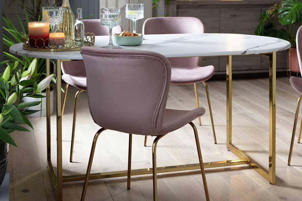 Image of an oval dining table with marble style top and gold legs.