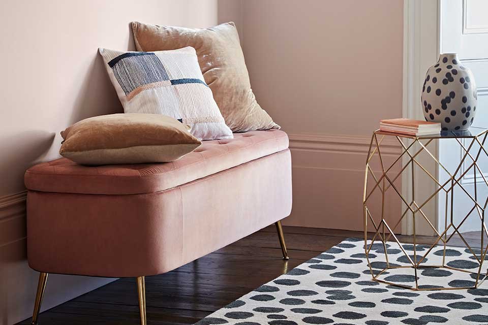 Pink velvet storage bench with cushions on top.