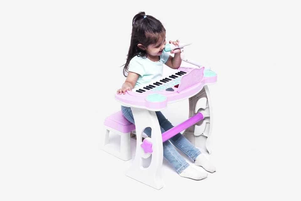 A girl singing into the mic on the Chad Valley keyboard stand and stool in pink and white.