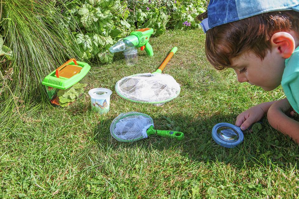 Boy looking through a magnifying glass in the garden using the Chad Valley nature explorer kit.