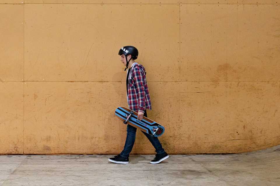 Boy in a helmet walking and holding his Airwalk mid skateboard in blue, black and brown.