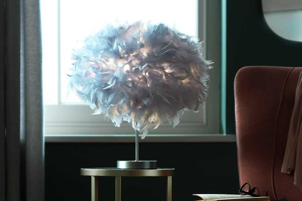 The Argos Home feather table lamp sitting on a bronze table behind an occasional chair.