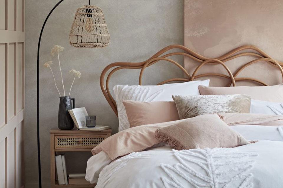 Bedroom with a rattan bed frame and floor lamp with white and pink bedding.