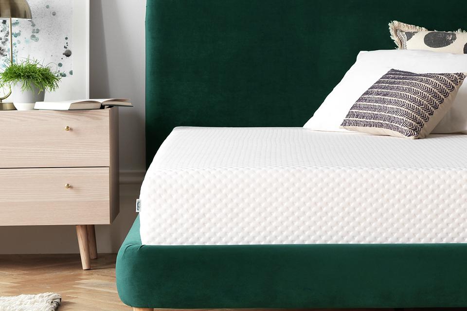A white mattress on green velvet bed frame in a bedroom.