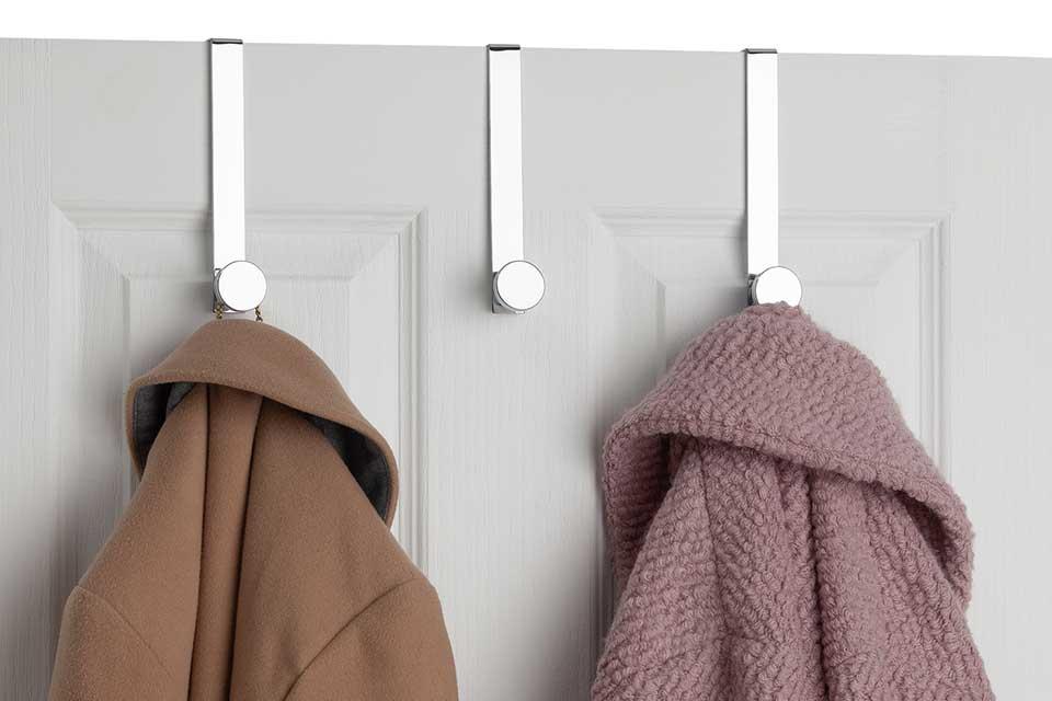 Three over the door stainless steel hooks with coats hanging from them.