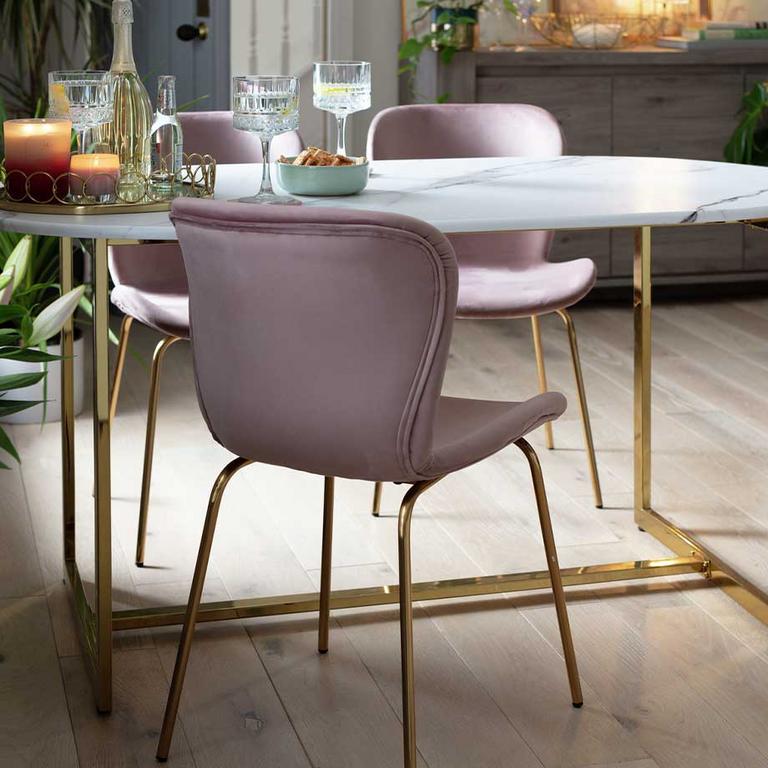 Image of pink velvet chairs around a marble and gold dining table. 