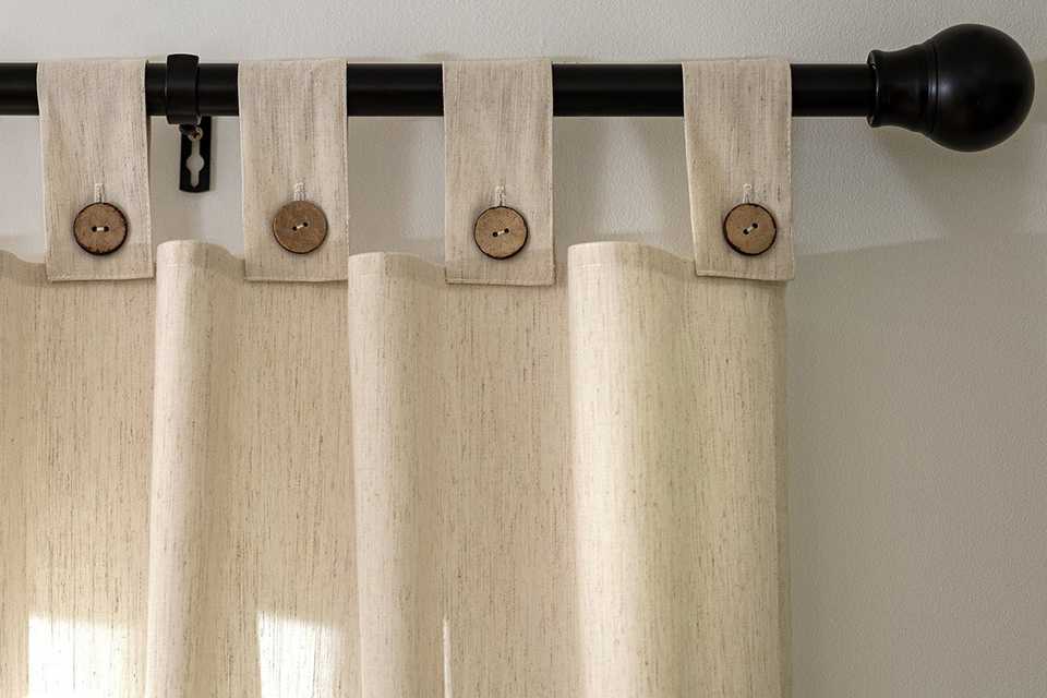 A Habitat button voile unlined tab top curtain hanging from the rail in a living room.