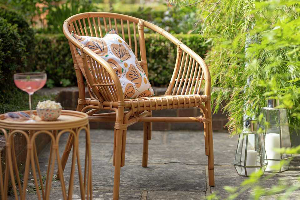 A rattan garden chair with a pillow sitting outdoors.