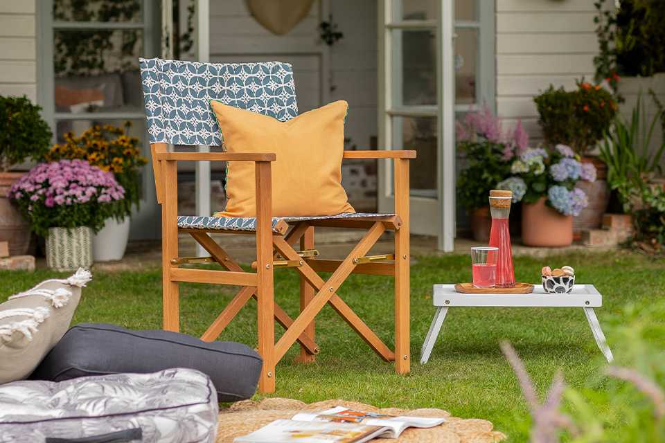 A wooden framed outdoor folding chair with an orange cushion on it. 