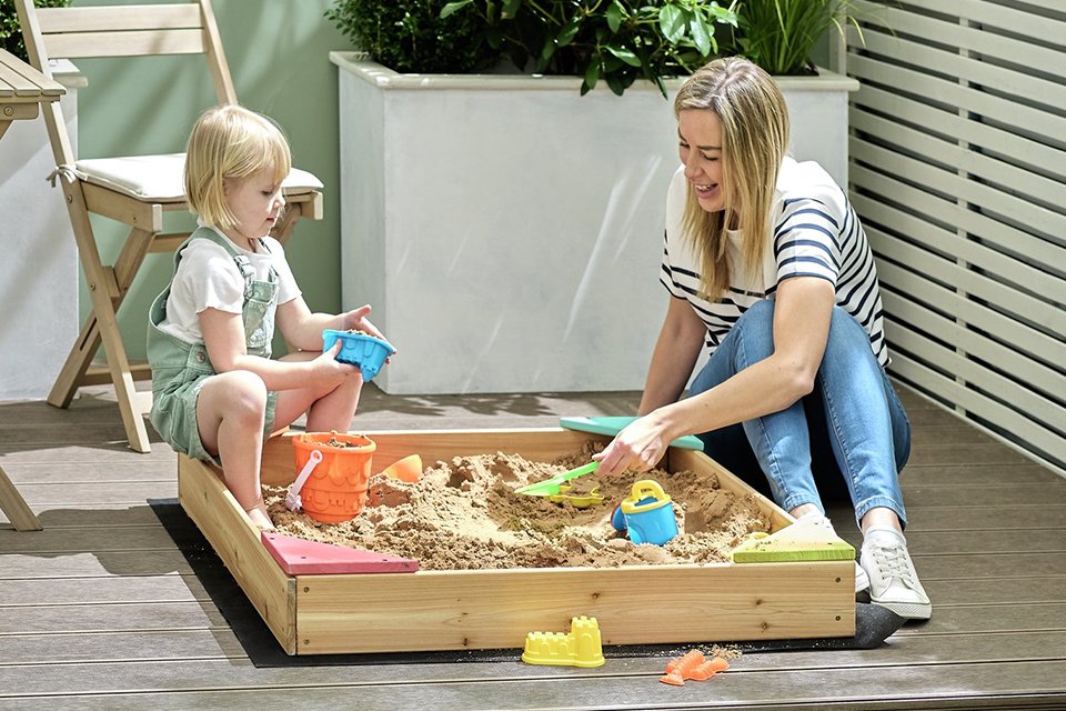 Mum and child playing outside in a wooden sand box