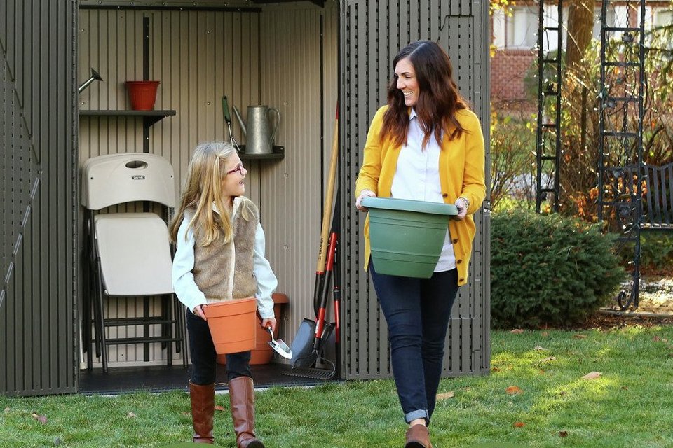 A mother and daughter bringing out planters out of a Lifetime plastic outdoor storage shed.