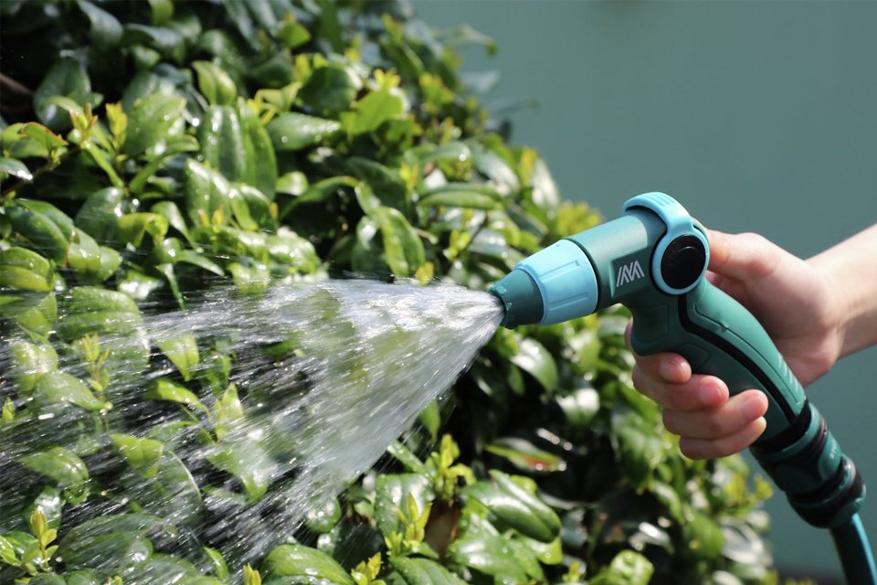 A person spraying water on plants using a McGregor garden hose sprayer.