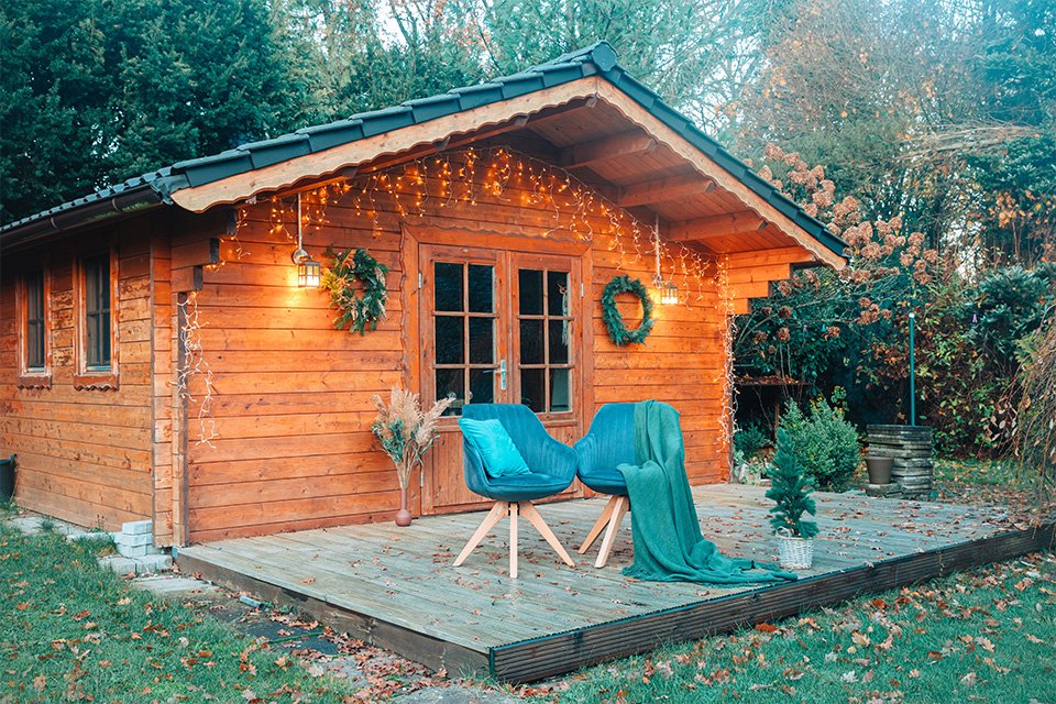 A wooden shed decorated with green plants and faux grass and lights.