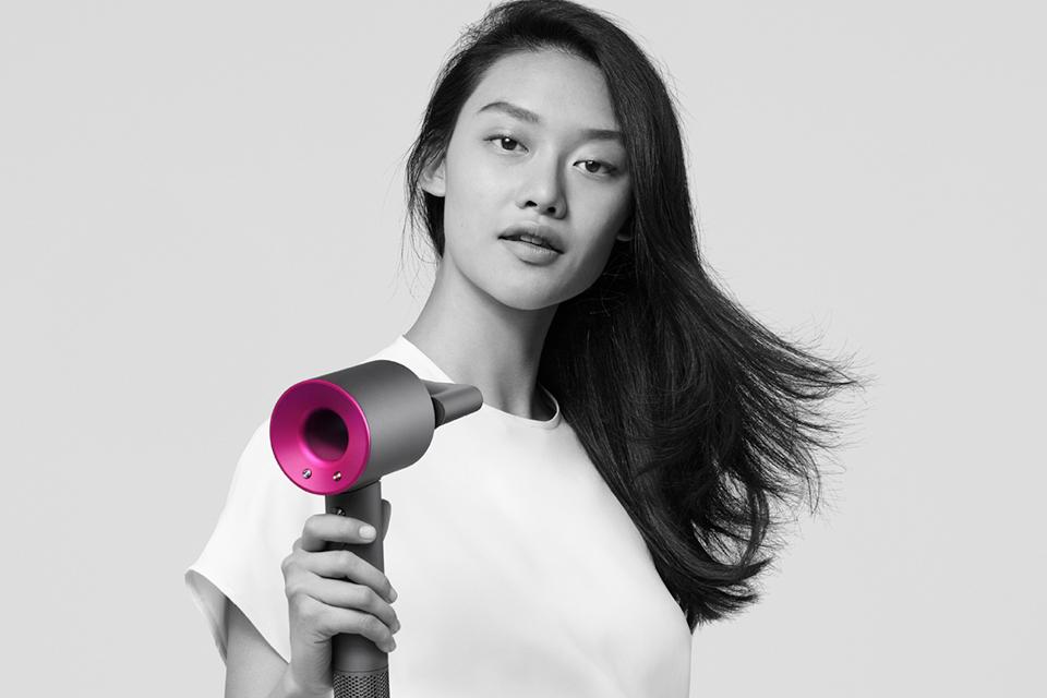 A lady drying her hair with the Dyson Supersonc hair dryer in fuchsia and black.