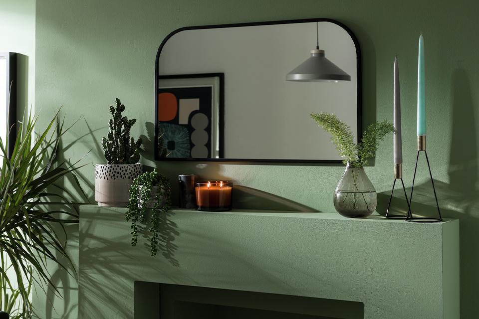Mirror above mantelpiece with plants and candles.
