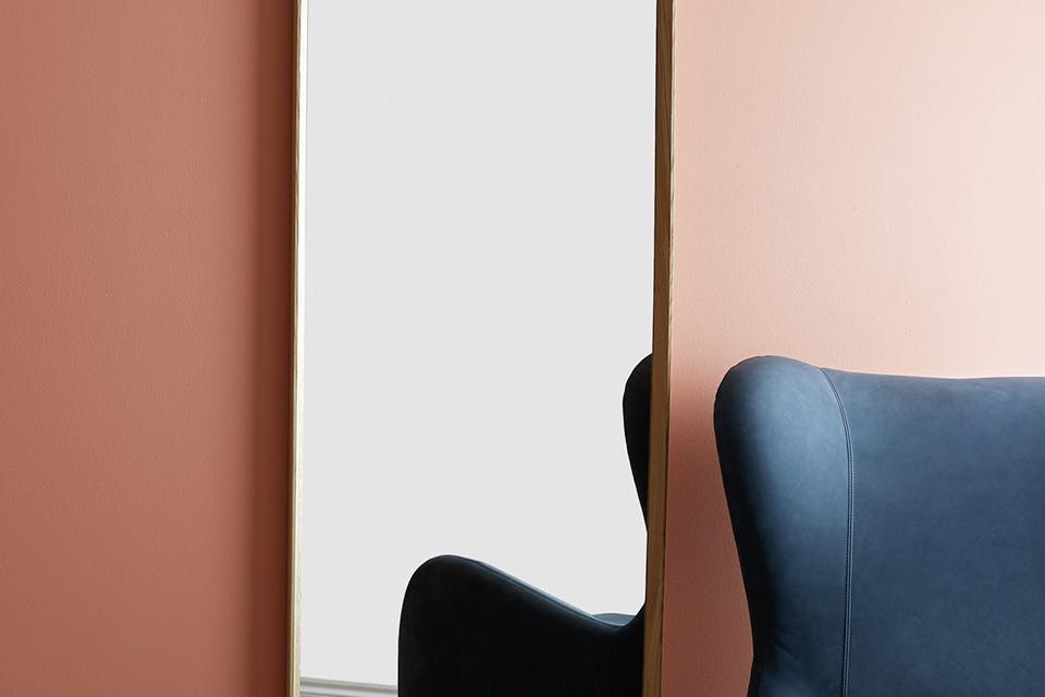 A walnut full-length mirror next to a blue armchair.