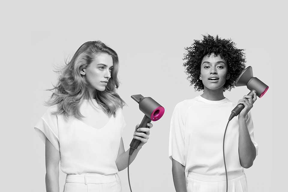 Two ladies drying their hair with the Dyson Supersonic. One has the diffuser attachment.