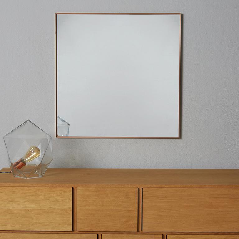 Gold square mirror above a wooden chest of drawers.