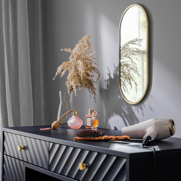 Gold oval mirror above a black dressing table with a hairdryer and perfumes.