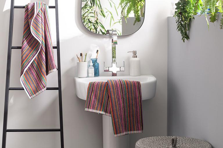 Multi-coloured towels displayed on a black towel ladder and white sink in a bathroom.