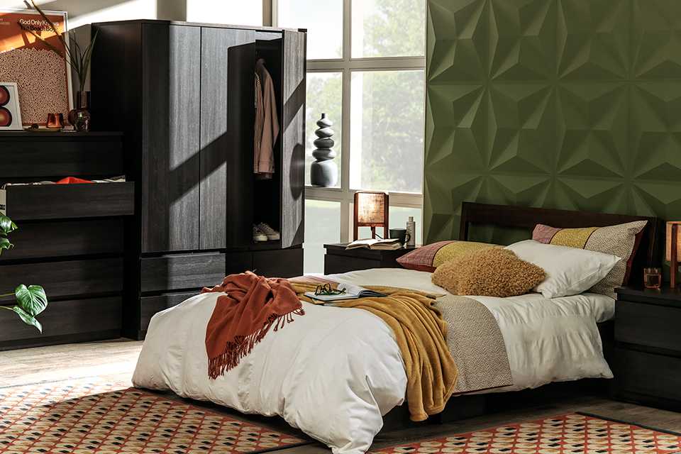 Charcoal black coloured wardrobe, drawers and a double bed in a bedroom.